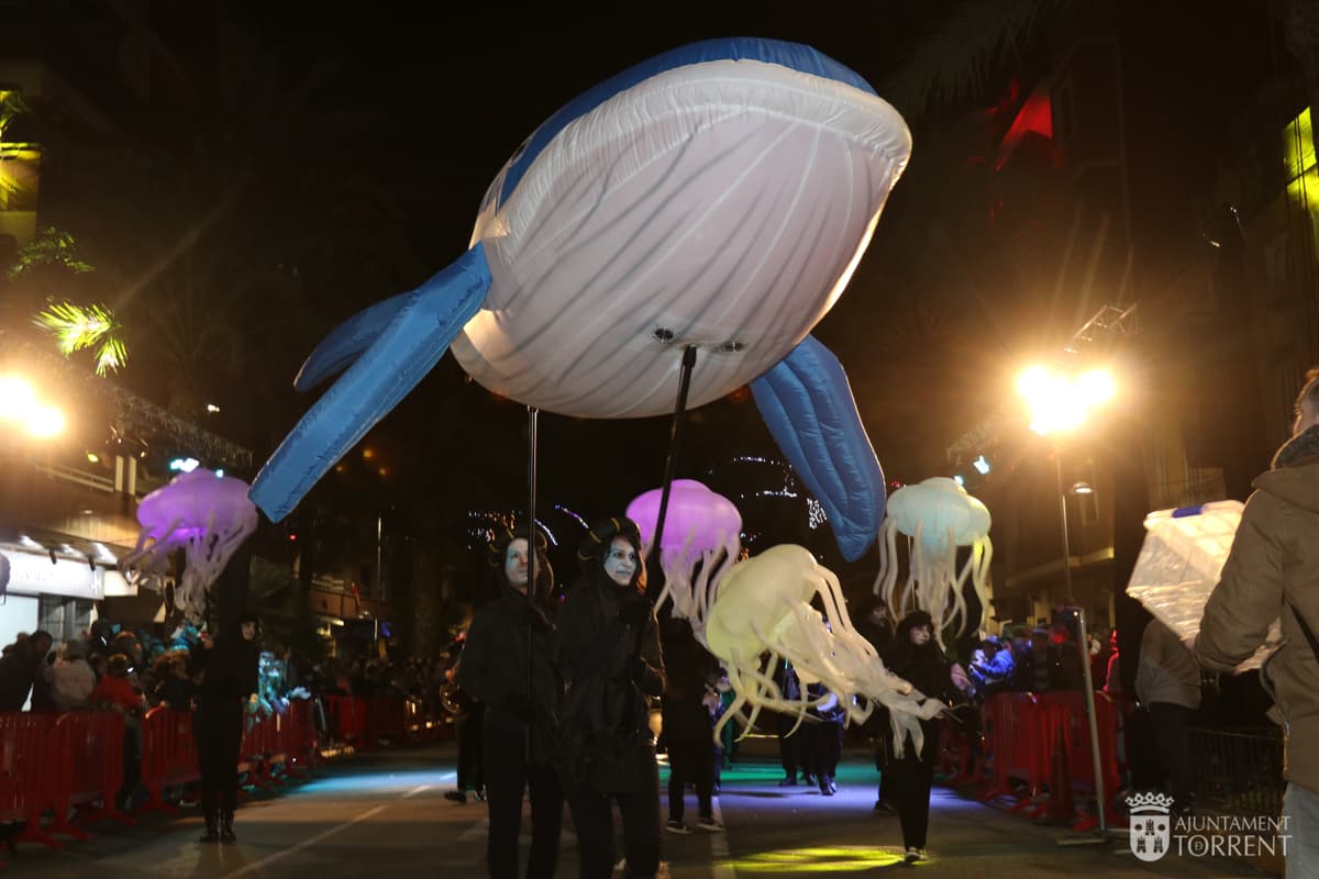 Ballena hinchable gigante flotando sobre un desfile nocturno con figuras de medusa iluminadas debajo