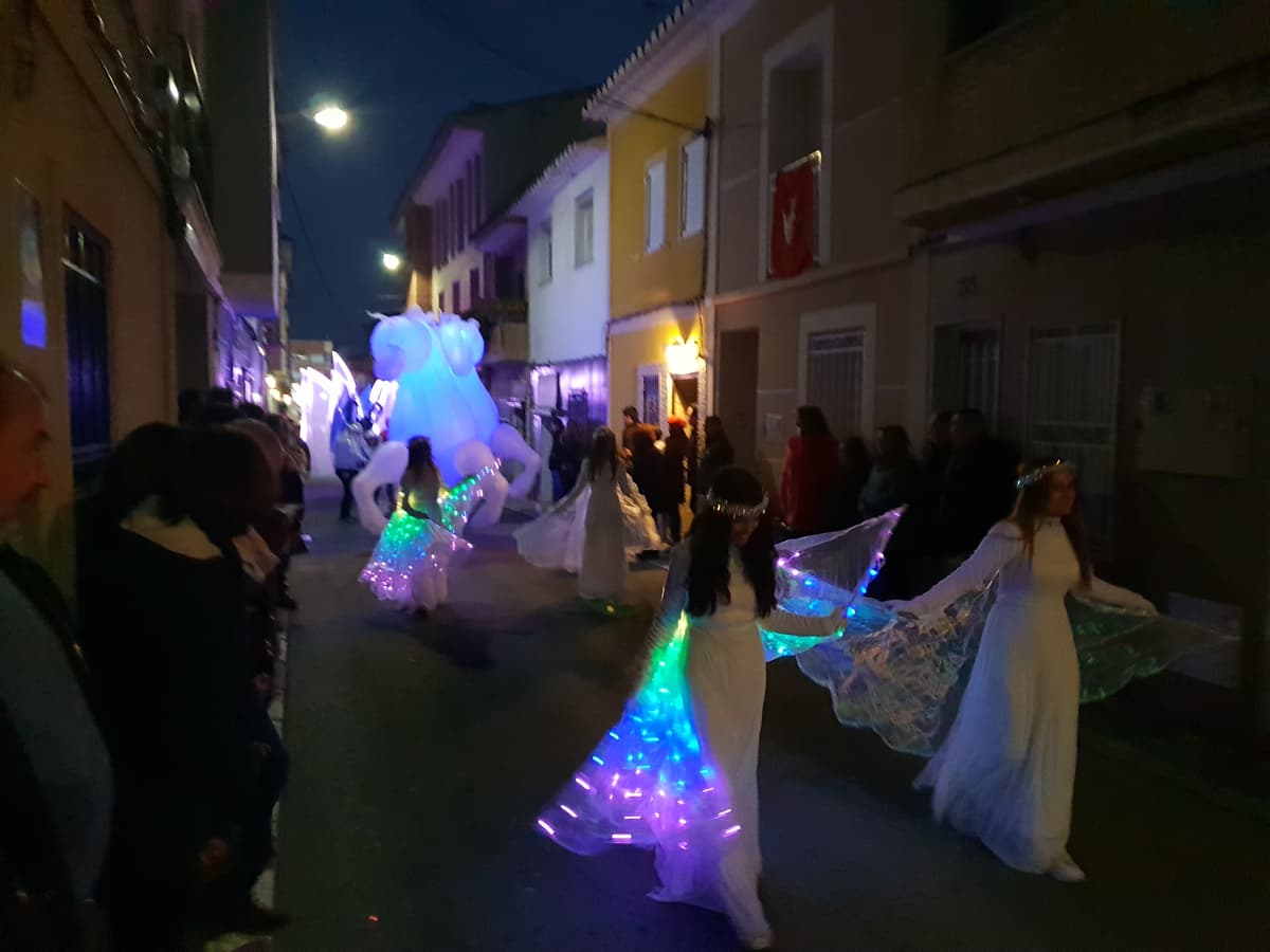 Figura hinchable de caballo iluminado detrás de artistas con vestuario led en un pasacalles nocturno