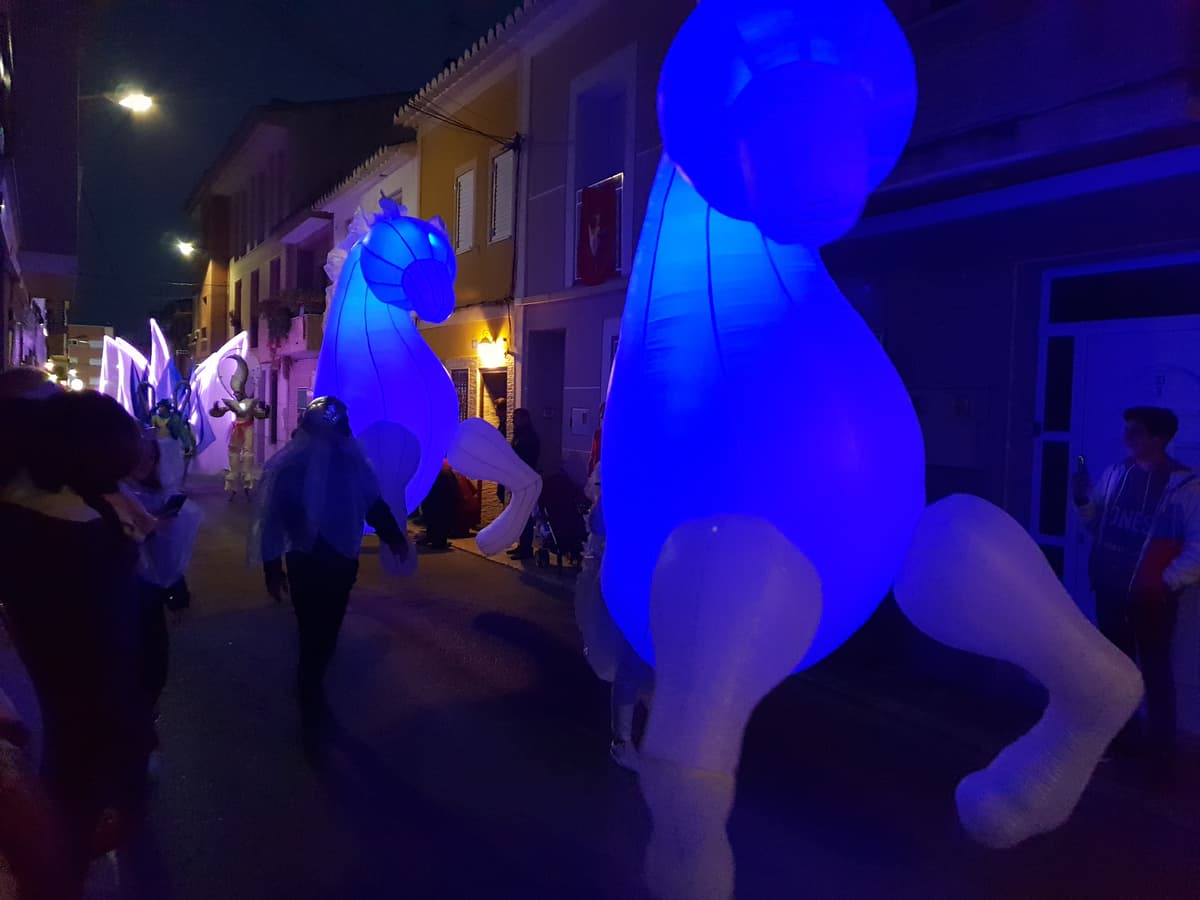 Caballos hinchables iluminados en azul avanzando por una calle estrecha de noche