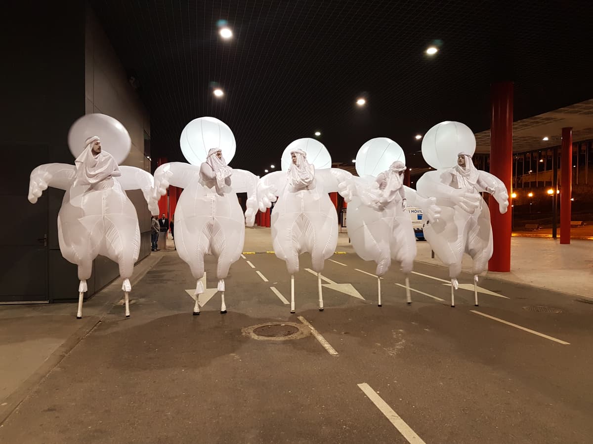 Cinco cabezudos hinchables blancos avanzando en cortejo nocturno por una calle