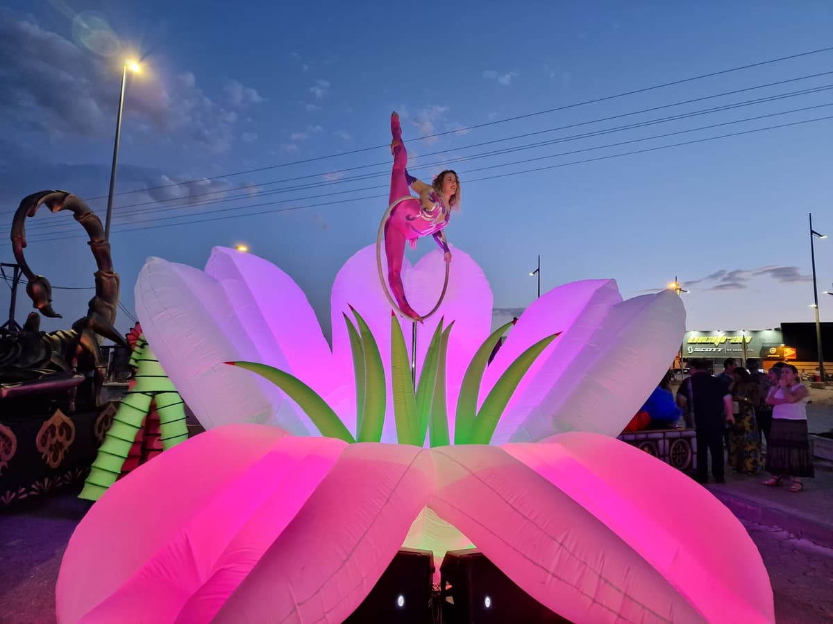 Carroza con flor hinchable gigante y acróbata suspendida en un aro sobre ella