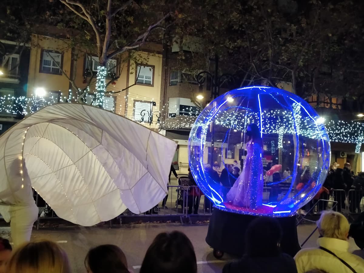 Esfera azul iluminada y elemento de concha blanca en una calle decorada con luces de Navidad