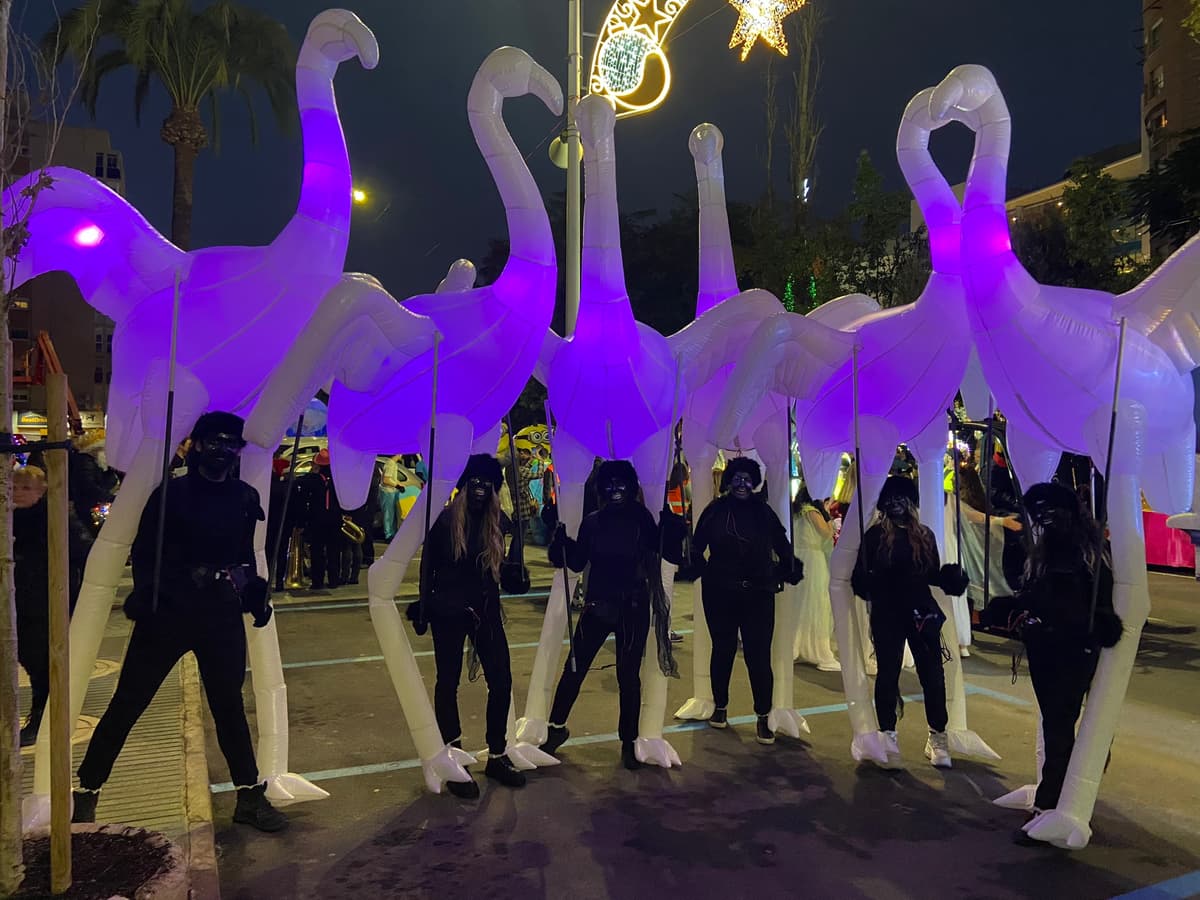 Hilera de flamencos hinchables de gran formato avanzando junto a su equipo de operarios en una calle nocturna