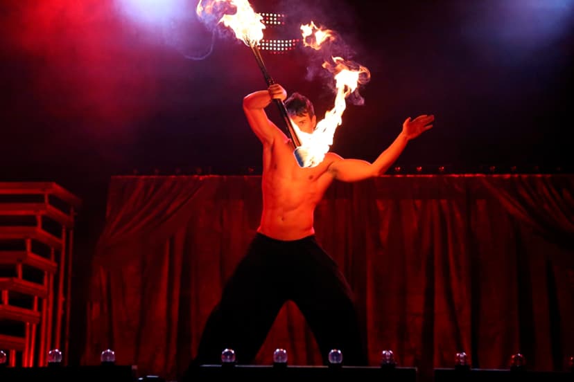 Artista de fuego escénico sosteniendo una vara de fuego encendida por los dos extremos frente a un telón rojo