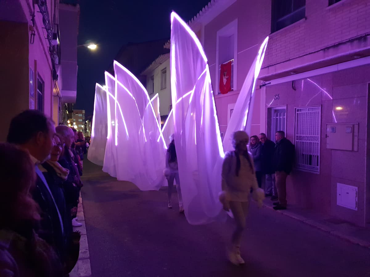 Grandes velos de tela con iluminación led morada avanzando por una calle estrecha en un pasacalles nocturno