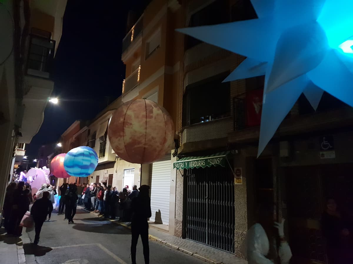 Esferas de planetas iluminadas junto a una estrella azul avanzando por una calle estrecha de noche