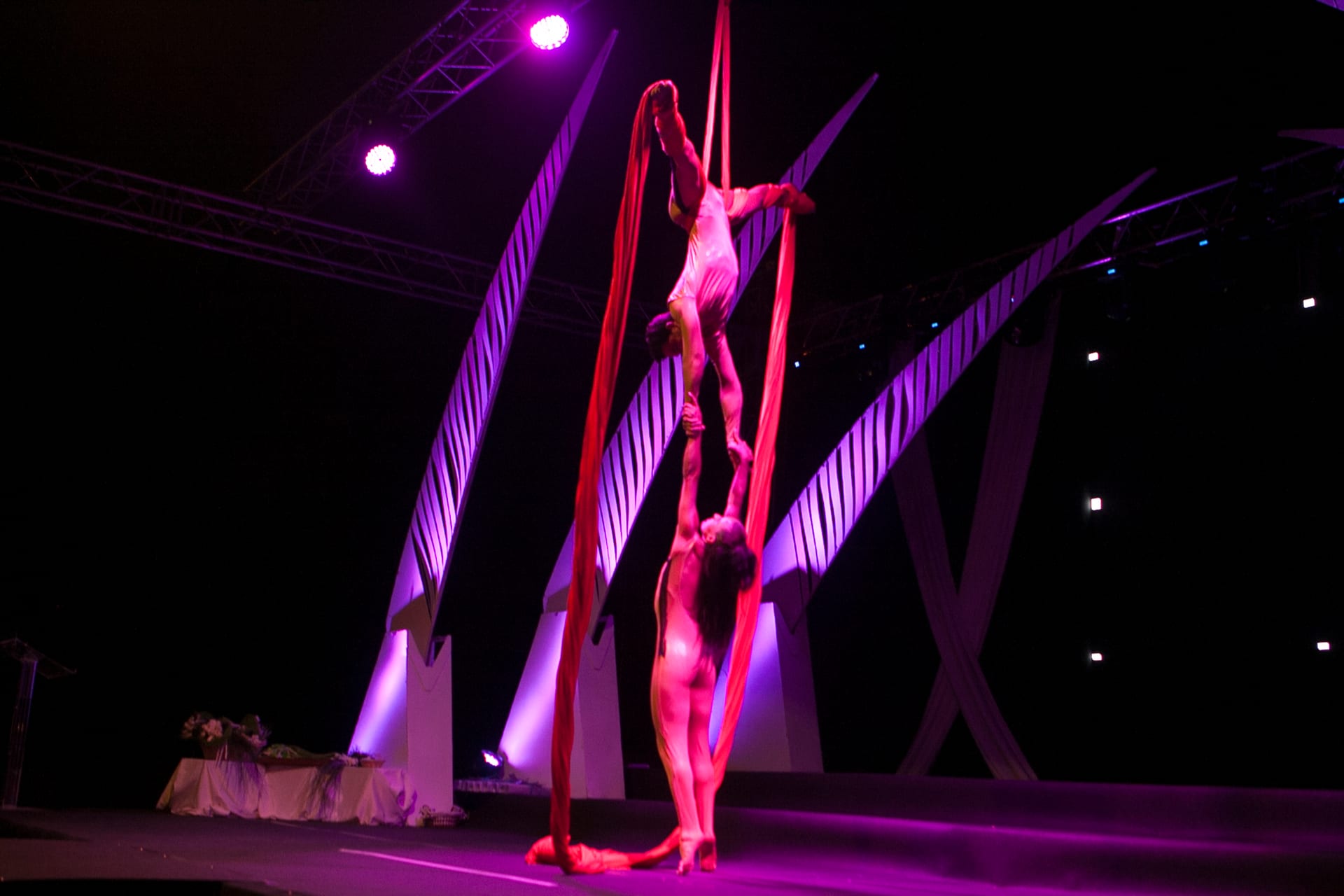 Acróbatas en telas aéreas rojas con iluminación escénica magenta y arquitectura escenográfica