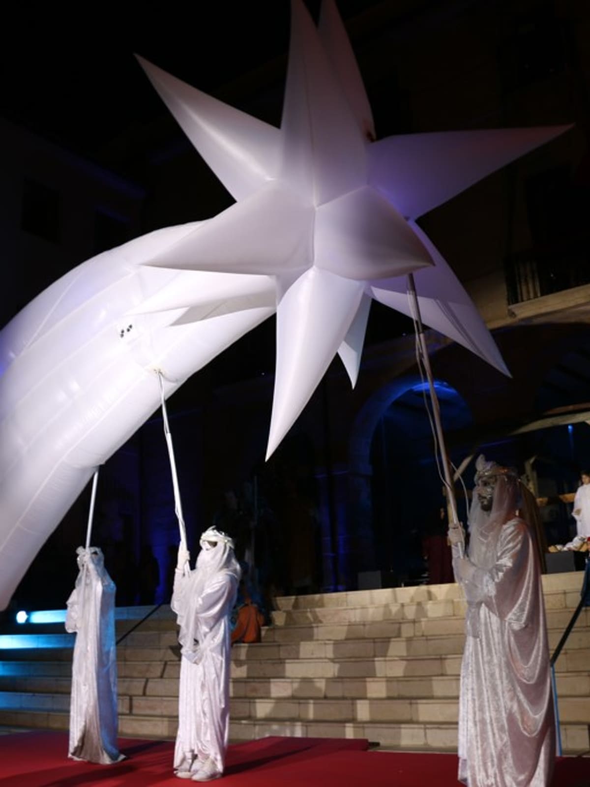 Estrella de Oriente hinchable gigante con cola de cometa sostenida por figurantes con vestuario blanco en cabalgata de Reyes